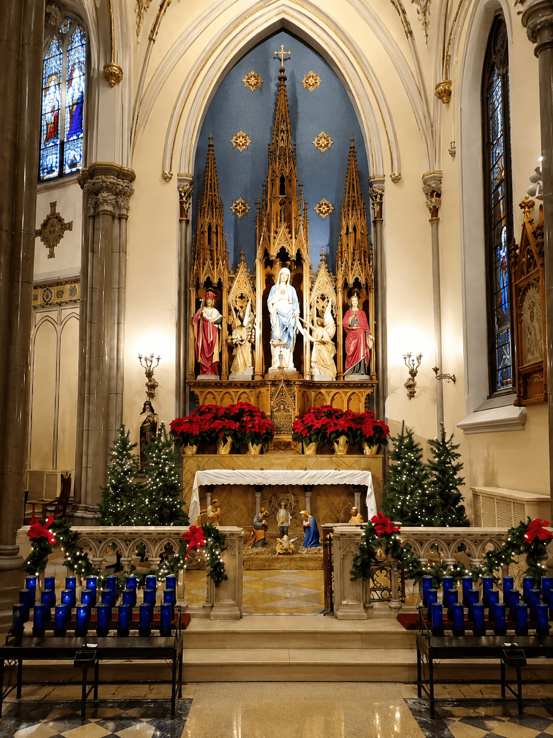 Virgin Mary statue on an ornate Gothic church altar with stained-glass windows, Christmas trees, red flowers and blue candles, 4K image.
