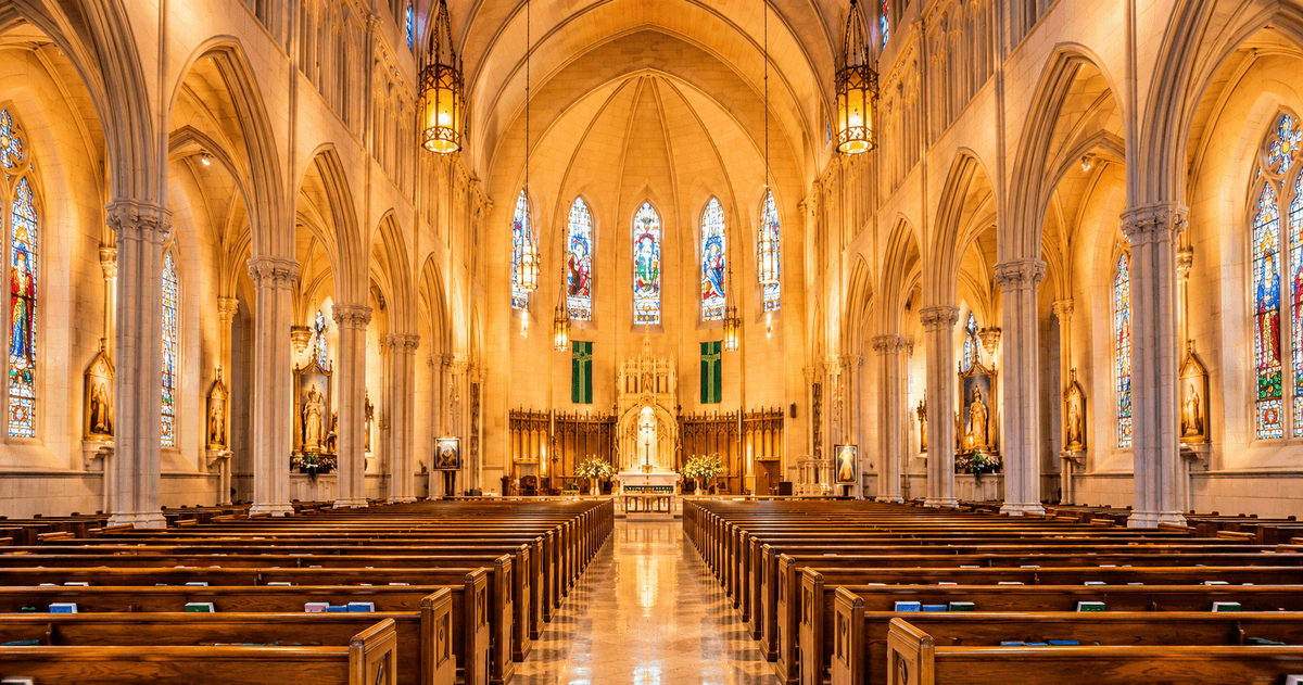 Grand cathedral interior with Gothic arches, stained glass windows, wooden pews, altar and warm golden lighting.